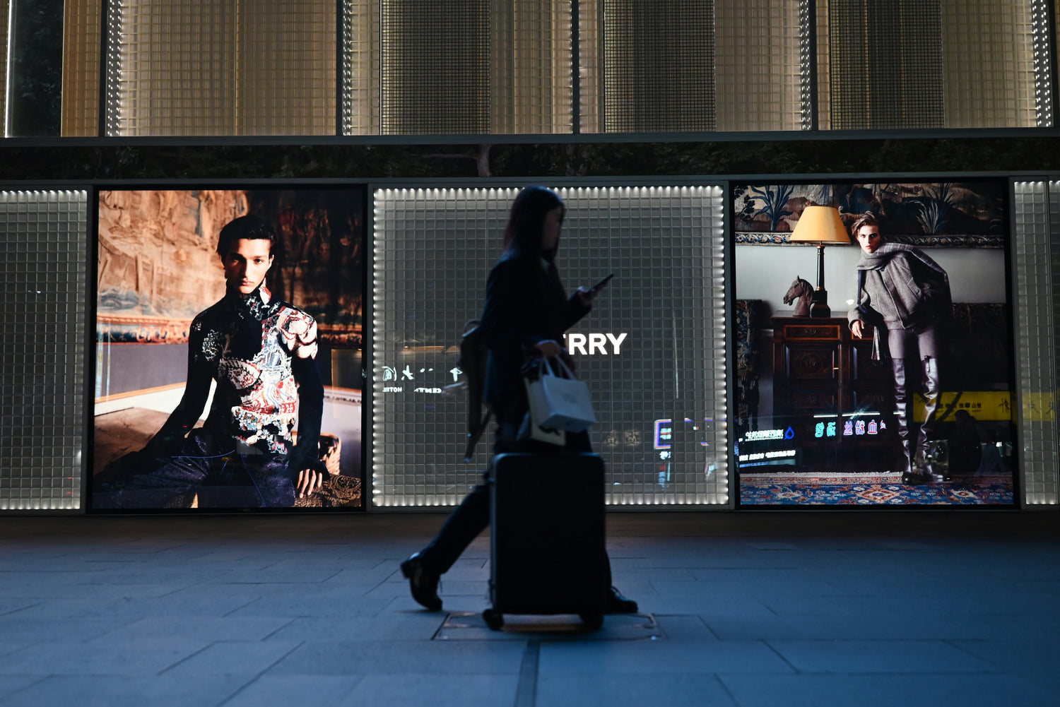 Person walking past a large screen displaying fashion advertisements.